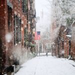 snow covered road between brown concrete buildings during daytime
