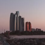 Capture of Abu Dhabi's skyline at dusk with a rocky beach foreground, highlighting modern architecture.
