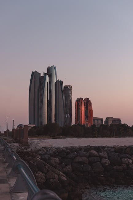 Capture of Abu Dhabi's skyline at dusk with a rocky beach foreground, highlighting modern architecture.