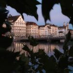 Buildings reflected in the water, framed by leaves.