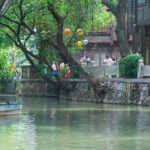 a boat floating down a river next to a lush green forest